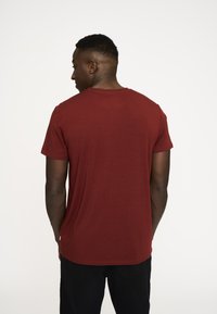 Mørkerød T-shirt med rund halsudskæring, korte ærmer og en glat tekstur, set bagfra uden synlige mønstre eller detaljer.