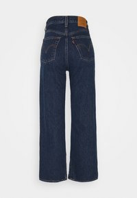 Jeans de mezclilla azul oscuro de pierna ancha con cintura alta, dos bolsillos traseros y una etiqueta de cuero marrón en la cintura. Tela texturizada.