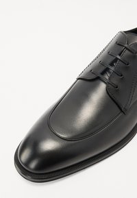 Scarpa da uomo in pelle nera con finitura liscia, punta affilata e design con lacci. Presenta cuciture fini e una suola in gomma testurizzata.