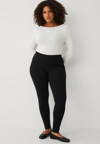Sorte leggings med en glat overflade, høj talje-design og kontrasterende side sømme. Sammen med en tætsiddende hvid langærmet top.