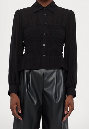 Black long-sleeve buttoned blouse with smocked waist and peplum hem paired with high-waisted black faux leather pants.