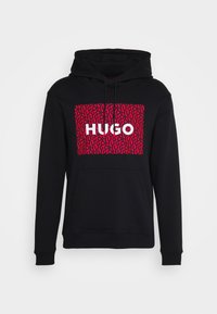 Černá mikina s kapucí a přední kapsou, obsahující velký červený grafický vzor a výrazn�ý bílý text "HUGO" uprostřed. Měkká tkanina, kapuce na šňůrku.