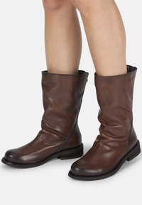Bottes de cheville en cuir marron au design décontracté, avec un bout arrondi et un petit talon empilé. Présente des coutures minimales et un doublage intérieur noir.