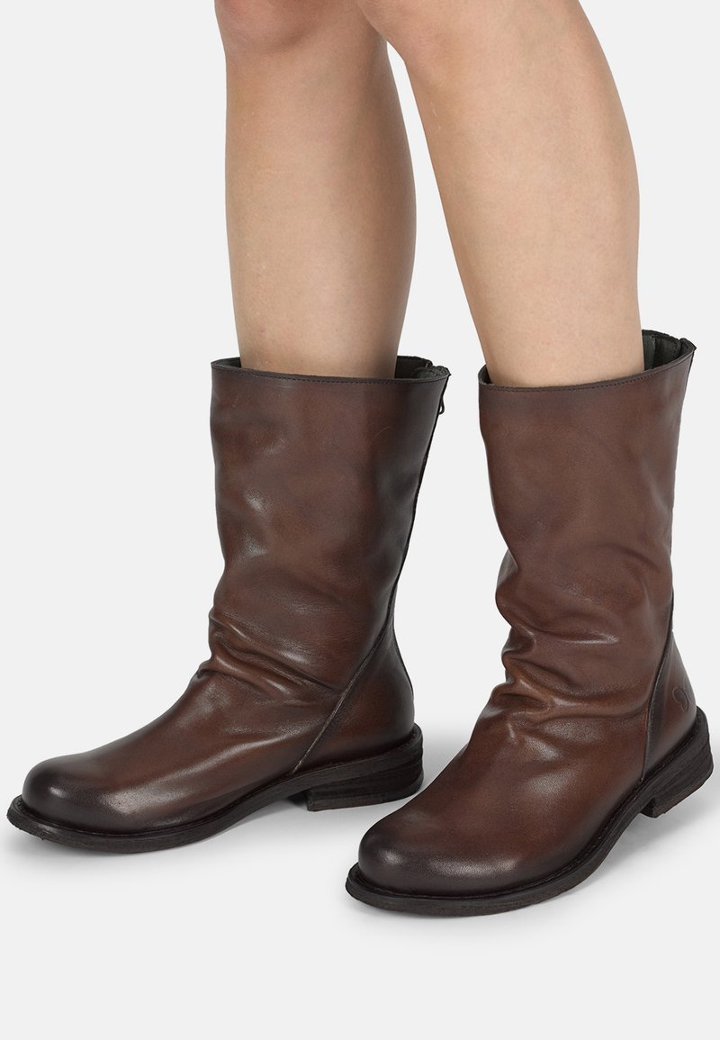 Bottes de cheville en cuir marron au design décontracté, avec un bout arrondi et un petit talon empilé. Présente des coutures minimales et un doublage intérieur noir.