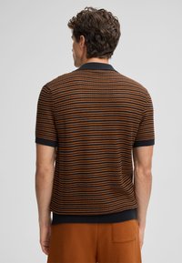 Polo a maglia con strisce nere, arancioni e blu. Maniche corte, colletto e orlo a coste, tessuto strutturato con finitura a motivo.