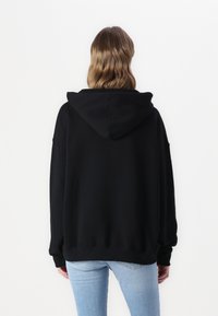 Sweat à capuche noir avec une coupe décontractée, doté d'un ourlet large et de manches longues, porté avec un jean ajusté bleu clair. Design minimaliste.