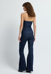 Granatowy, dwuczęściowy zestaw odzieżowy z strapless topem o dopasowanym kroju i rozszerzanymi spodniami. Kontrastowe szwy w całym zestawie.