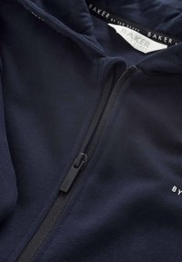 Mörkblå zip hoodie i texturerad tyg, med en svart dragkedja med ett "B"-handtag, och en etikett som säger "BAKER by TED BAKER."