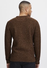 Pulover tricotat maro cu un corp texturat și tiv striat, având detalii de tricot cu cablu pe mâneci. Gât simplu de tip crew.