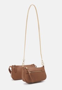 Brown leather crossbody bag with a gold chain strap, featuring a zippered pocket and smooth texture. Compact, with rounded sides.