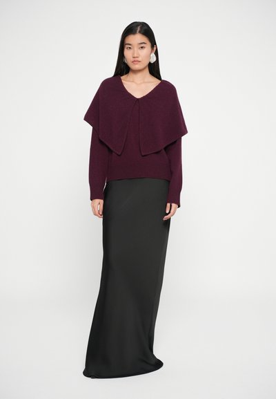 Maglione tricot bordeaux con scollatura a V e design sovrapposto e drappeggiato abbinato a una gonna lunga nera liscia. L'outfit presenta maniche lunghe e una silhouette aderente.