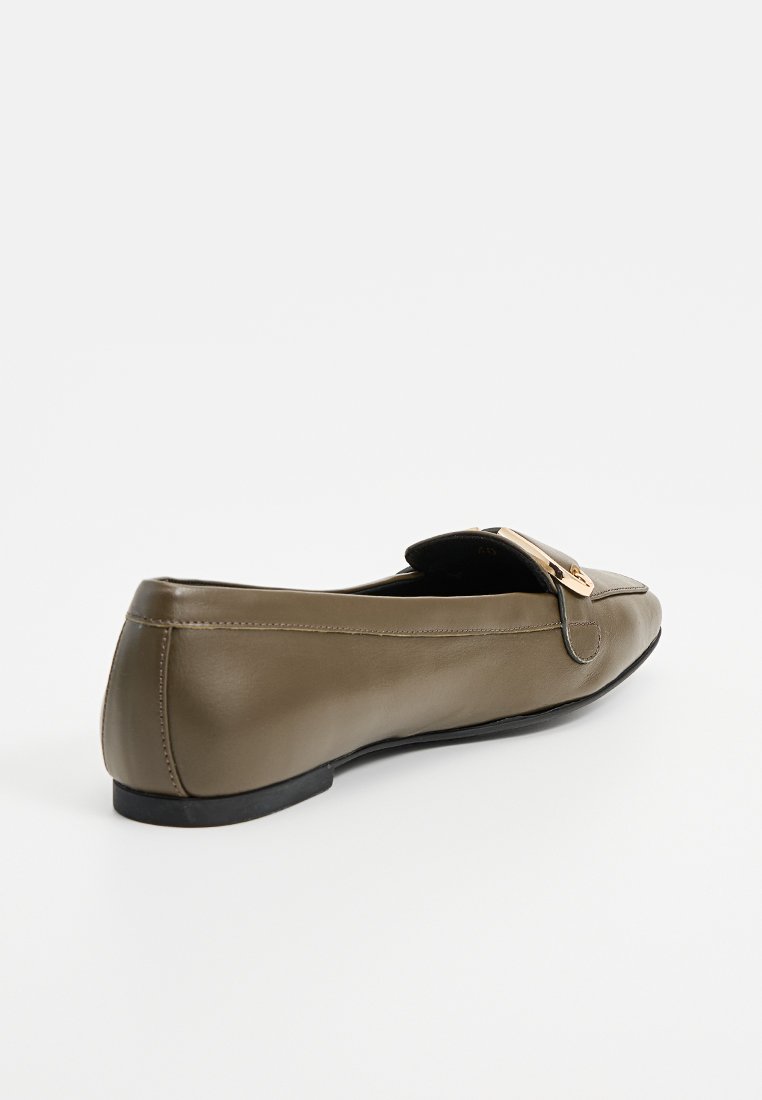 Chaussure plate en cuir vert olive avec un bout arrondi, semelle noire basse et une boucle dorée en accent sur le dessus. Texture lisse avec un design minimaliste.