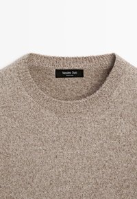 Maglione beige realizzato in un morbido tessuto a maglia. Collo a giro con bordi a costine. L'etichetta riporta "Massimo Dutti." Aspetto texture con leggere variazioni.