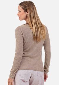 Haut à manches longues beige en tissu doux et texturé, avec un col rond et une coupe décontractée, porté avec un pantalon de couleur claire.