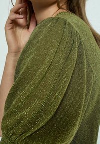 Olivgrön topp med texturerat, skimrande tyg. Långa puffärmar med insamlingar och en något figursydd form.