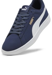 Marineblå sneakers med et glat stofoverdel, hvide accenter, snøredesign, fremtrædende Puma-logo i guld og en hvid gummisål.