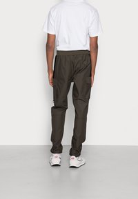 Cargo-Hosen in Olivgrün mit lockerem Schnitt, mehreren Seitentaschen und elastischem Bund. Kombiniert mit einem weißen T-Shirt und Sneakers.