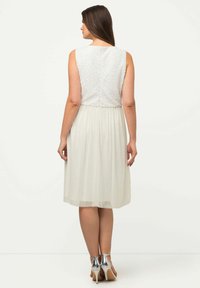 Valkoinen mekko, jossa on teksturoitu bodice ja levenevä sifonkihame, varustettuna takavetoketjulla ja polvipituudella. Hopeiset korkokengät täydentävät asustusta.