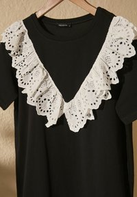 Czarny t-shirt z białą koronkową falbaną na szyi z misternymi wzorami wyciętymi, krótkimi rękawami i okrągłym dekoltem.