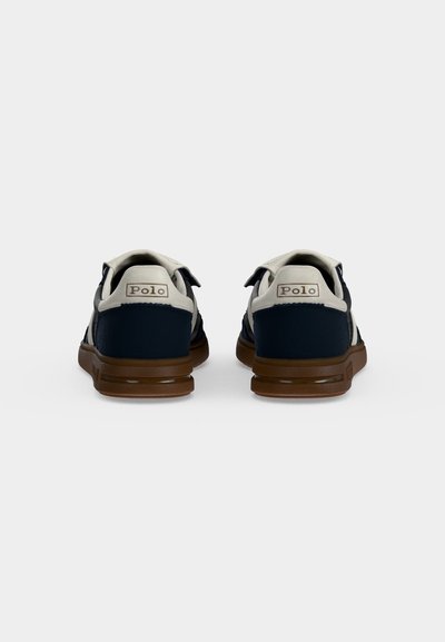 Ζευγάρι navy και λευκά sneakers χαμηλού παπουτσιού με καφέ σόλες, εμφανιζόμενα από πίσω, με λογότυπο "Polo" στην ταμπέλα της φτέρνας.