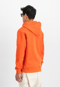 Sudadera con capucha de forro polar naranja brillante, con puños y dobladillo acanalados. Textura suave, corte holgado y minimalismo en los detalles.