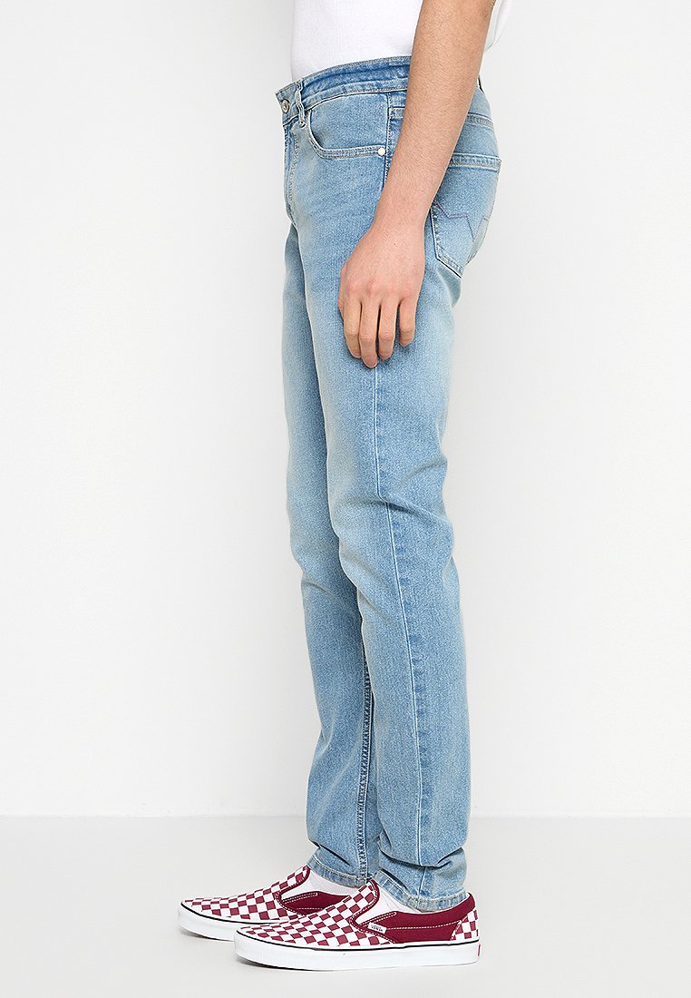 Vaqueros de denim azul claro con corte ajustado, que presentan un diseño clásico de cinco bolsillos, un sutil desgaste y combinados con zapatillas a cuadros burdeos y blancas.