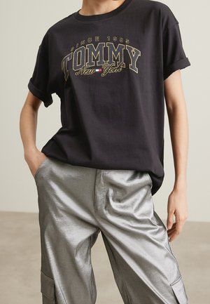 Czarny t-shirt z krótkim rękawem z złotymi i białymi napisami "TOMMY New York". W połączeniu z błyszczącymi, szerokimi, srebrnymi spodniami.