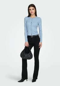 Haut bleu clair à manches longues avec boutons, jean noir ajusté, sac à main noir arrondi et escarpins pointus, sur un fond uni.