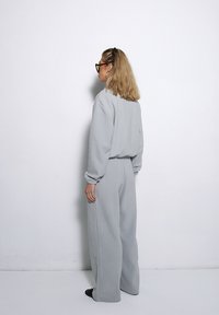 Szary, oversize'owy sweatshirt i dopasowane wysokie spodnie z miękkiego materiału, z długimi rękawami i elastycznymi mankietami. Prosty, luźny fason.