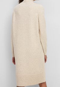 Beige gestricktes Kleid mit hohem Kragen, langen Ärmeln und geripptem Saum, das eine lockere Passform und eine weiche Textur aufweist.