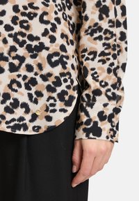 Leopardenmuster Bluse aus beigem, schwarzem und braunem Stoff; mit einem abgerundeten Saum und geknöpften Ärmeln, verziert mit einem subtilen goldenen Akzent.