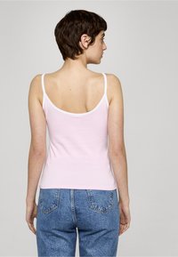 Svetloružové tielko s bielym lemovaním, tenkými ramienkami a priliehavým strihom. Nosené s modrými riflemi s vysokým pásom.