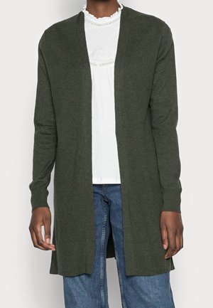 Long dark green open-front cardigan worn over a white ruffled blouse and blue jeans, shown from neck to mid-thigh.
