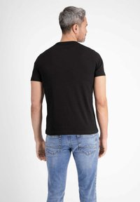 Black cotton t-shirt with short sleeves, fitted design, and a crew neckline, displayed on a male model wearing light blue jeans.