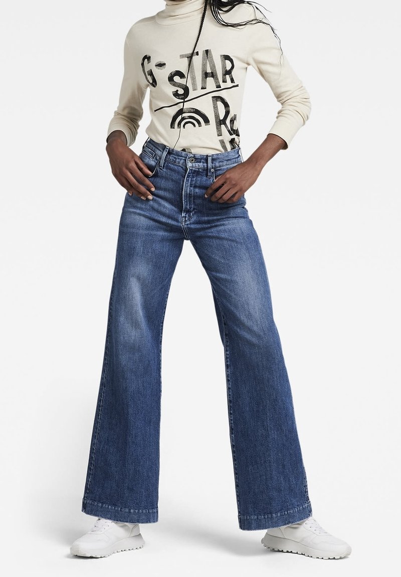 Vida jeans i medium blåtvätt med vida ben och hög midja, samt en traditionell femfickdesign. Matchas med en gräddfärgad långärmad topp med grafik.