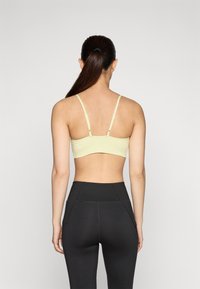 Reggiseno sportivo giallo chiaro con spalline regolabili, caratterizzato da un design senza cuciture e una texture morbida. Abbinato a leggings neri a vita alta.