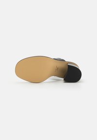Sandal de tacón negro con un material superior suave, que presenta un diseño sencillo, suela beige y detalles plateados en la correa.