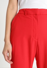Rote, hochtaillierte Hosen mit glatter Textur, ausgestattet mit vorderen Taschen und einer maßgeschneiderten Passform. Keine sichtbaren Beschläge oder Muster.