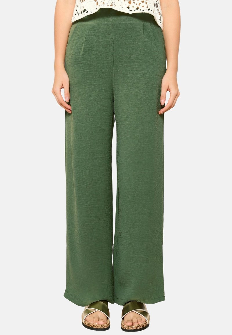 High-waisted, wide-leg green trousers made of textured fabric with side pockets. Worn with flat sandals featuring a metallic strap.