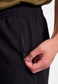 Schwarze Jogginghosen aus einem strukturierten Stoff, mit einer Reißverschlusstasche an der Seite und einem elastischen Bund für eine verstellbare Passform.