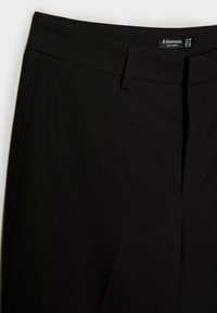 Pantalon noir sur mesure avec ceinture, passants de ceinture et fermeture éclair à l'avant, étiqueté Stradivarius, fabriqué au Cambodge.
