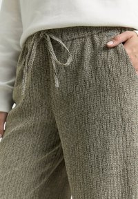 Textuurige, lichtbruine broek met een subtiel patroon, elastische tailleband en aantrekkoord. Zijzak zichtbaar, gemaakt van zachte stof.