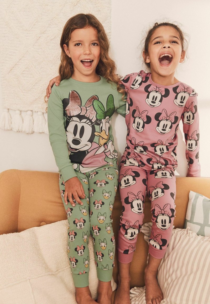 Two children wear coordinating pajamas. One is green with Disney character prints; the other is pink with Minnie Mouse faces. Soft cotton material.