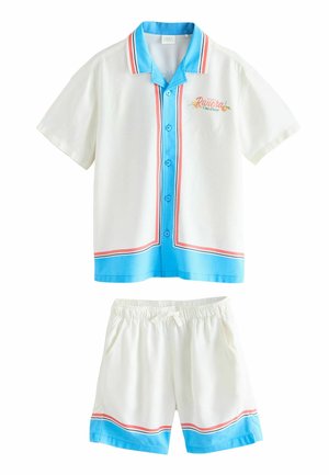 Camicia bianca a maniche corte con bottoni e pantaloncini con vita elastica con bordino a righe blu e rosse e scritta "Riviera Côte d'Azur" sulla camicia.