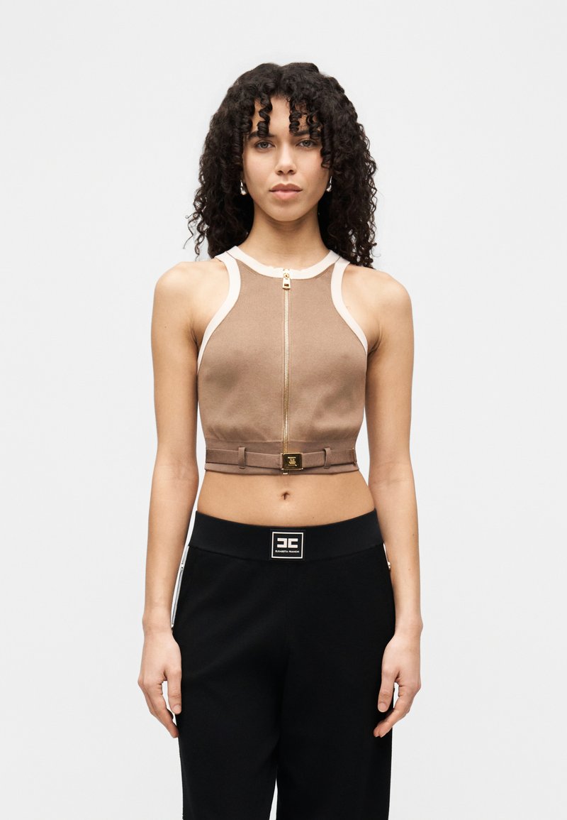 Καφέ κομμένο τοπ με λευκές πινελιές, με φερμουάρ στο μπροστινό μέρος και ζώνη με χρυσές λεπτομέρειες. Συνδυάζεται με μαύρο παντελόνι.