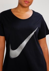 Mustapaita, jossa on pyöreä kaula-aukko ja lyhyet hihat. Paidassa on edessä suuri valkoisilla raidoilla varustettu Nike-swoosh-logo.