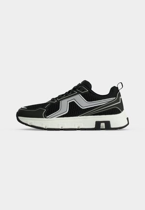 Chaussure de sport en mesh noir avec des touches blanches et grises, semelle blanche épaisse et languette au talon, vue de profil sur fond uni.