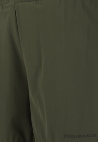 Vattentålig grön sportjacka i slät tyg, med en subtil lyster, elastisk fåll och "ENDURANCE"-logotyp i svart på sidan.