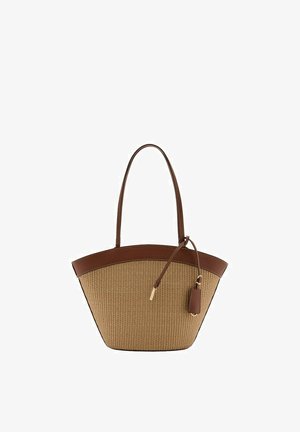 Bolso tote con cuerpo tejido beige, ribetes de cuero marrón, asas largas y una etiqueta de cuero colgando de una correa delgada en el lateral.