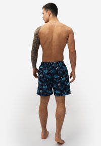 Heren zwembroek in marineblauw met een tropische print. Gemaakt van lichtgewicht stof, met een elastische tailleband en een relaxte pasvorm.